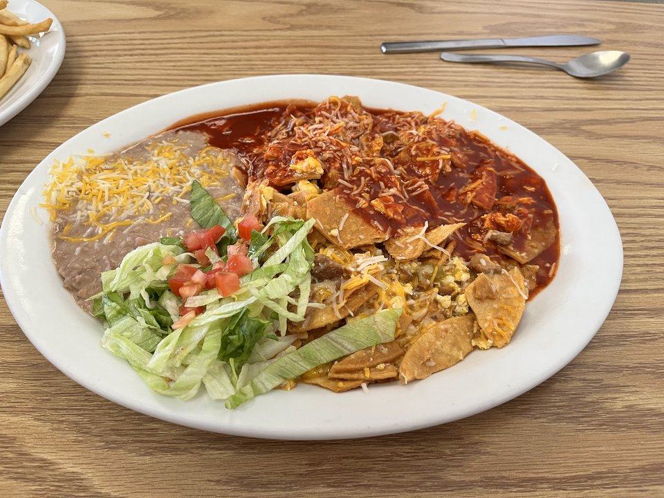 A plate with red sauce over chips and egg, refried beans, shredded lettuce, and tomato.